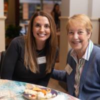 Katherine Boozer and Linda Vasilaki sitting at table, smiling at camera